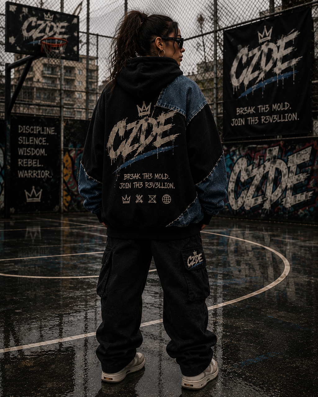 Female model wearing CZDE Denim Patchwork Hoodie – back view showing BR3AK TH3 MOLD manifesto graphic on basketball court