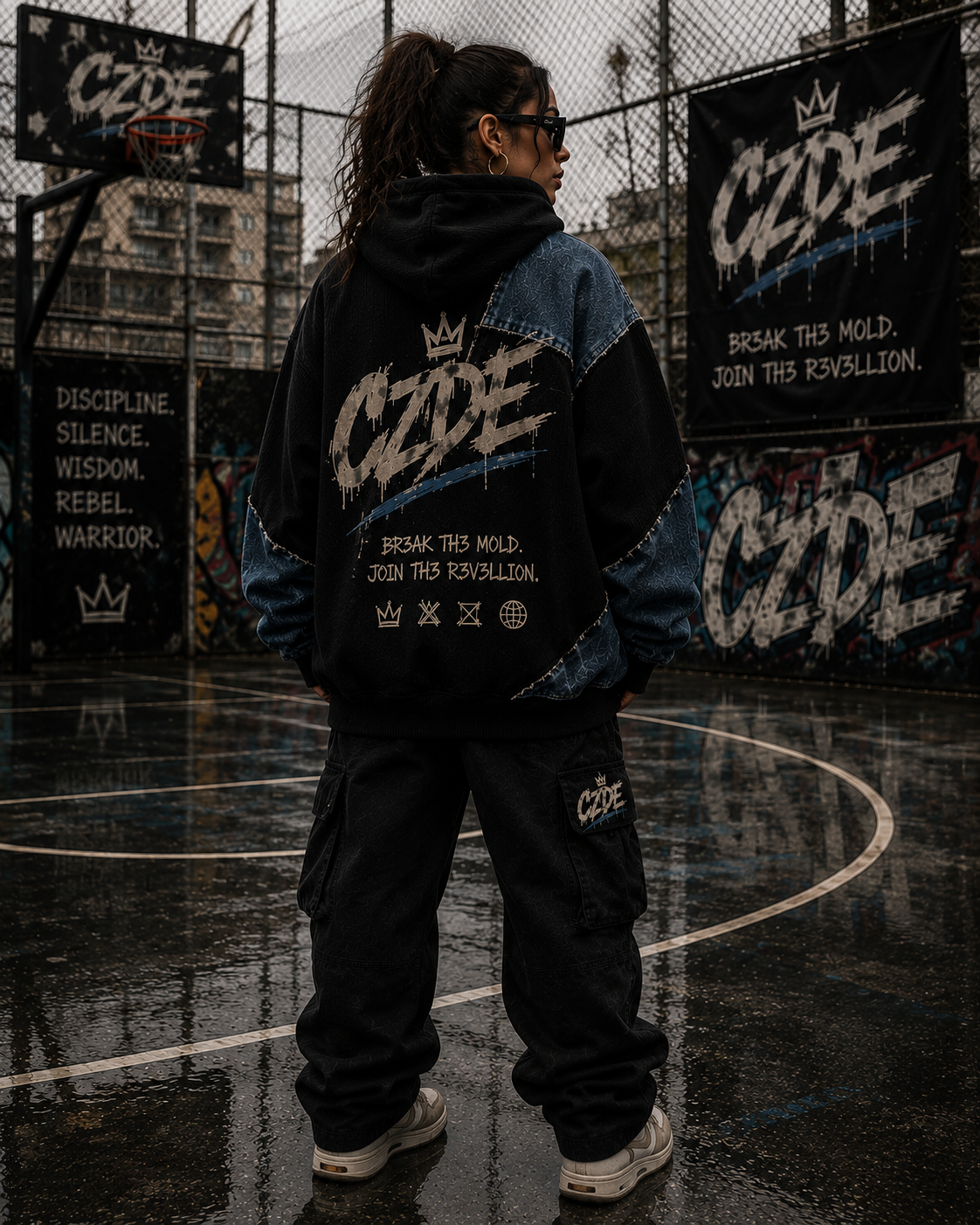 Female model wearing CZDE Denim Patchwork Hoodie – back view showing BR3AK TH3 MOLD manifesto graphic on basketball court