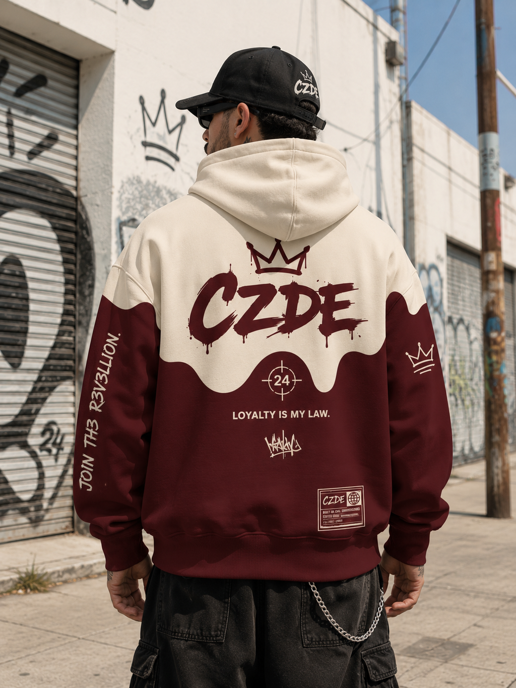 Male model wearing CZDE Burgundy Drip Hoodie – back view showing LOYALTY IS MY LAW print and CZDE crown, graffiti wall street editorial