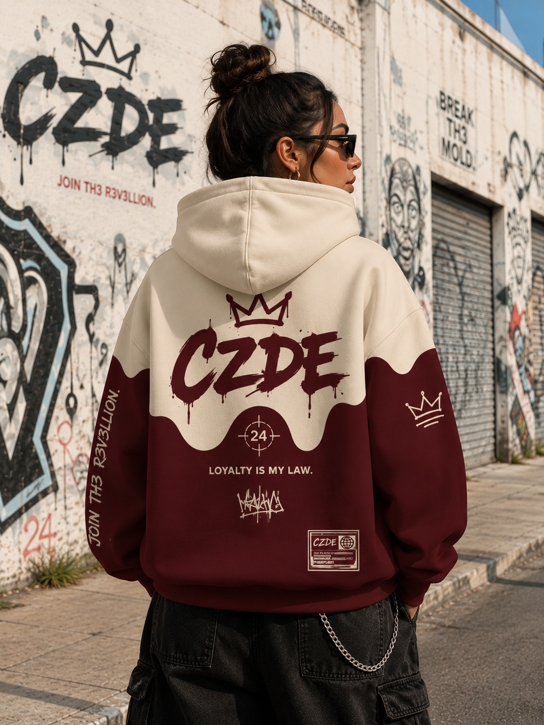 Female model wearing CZDE Burgundy Drip Hoodie – back view showing LOYALTY IS MY LAW print, JOIN TH3 R3V3LLION graffiti wall editorial