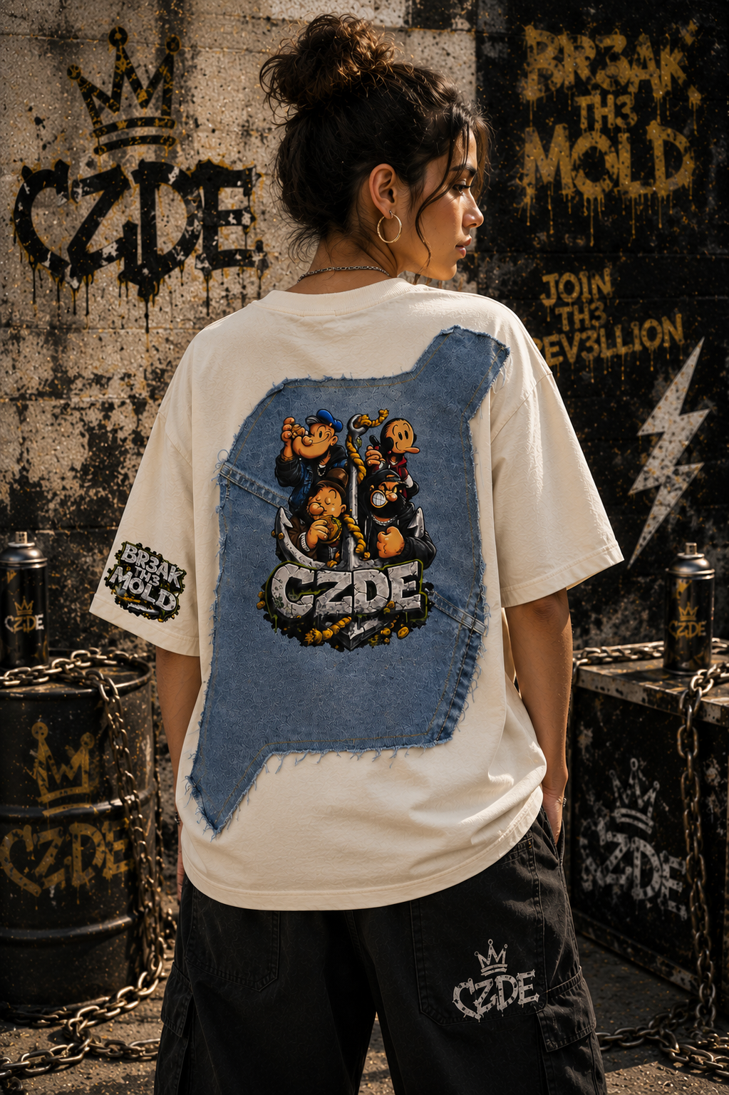 Female model wearing CZDE x Popeye Denim Patch Tee – back view showing full Popeye crew denim panel print, JOIN TH3 R3V3LLION graffiti wall editorial