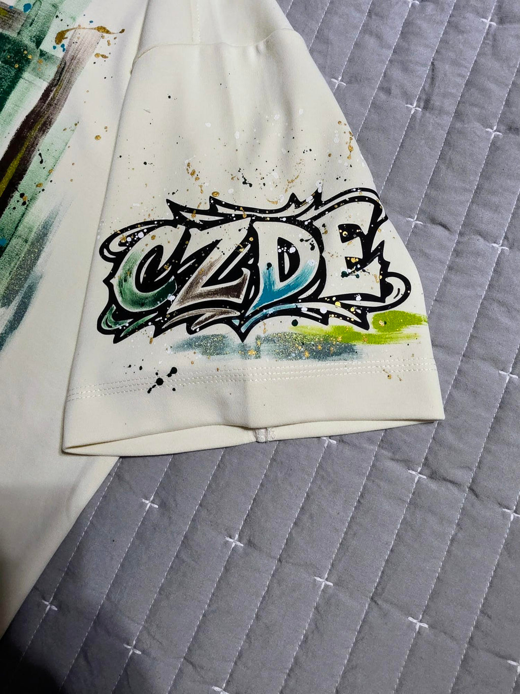 CZDE graffiti logo sleeve detail – teal and neon yellow hand-painted lettering